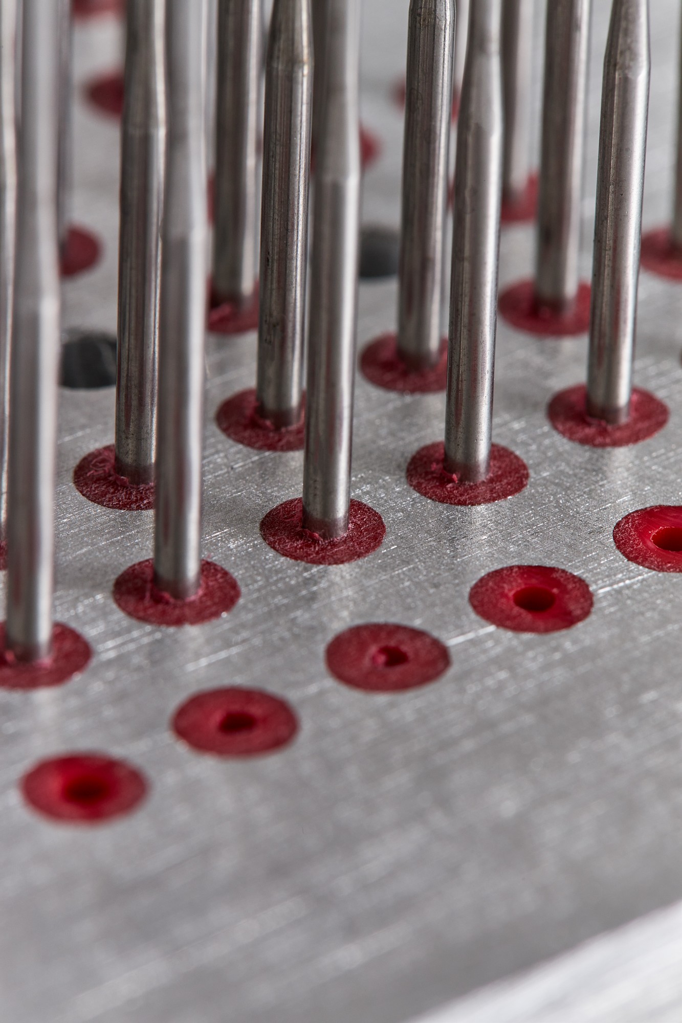 Close-up of an aluminium needle board with red inserts and steel needles